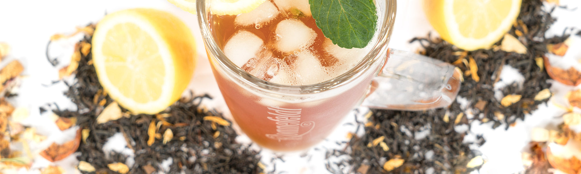 Eistee im Glas mit Eiswürfeln, Zitrone und Minze, umgeben von Schwarztee und Fruchtstücken