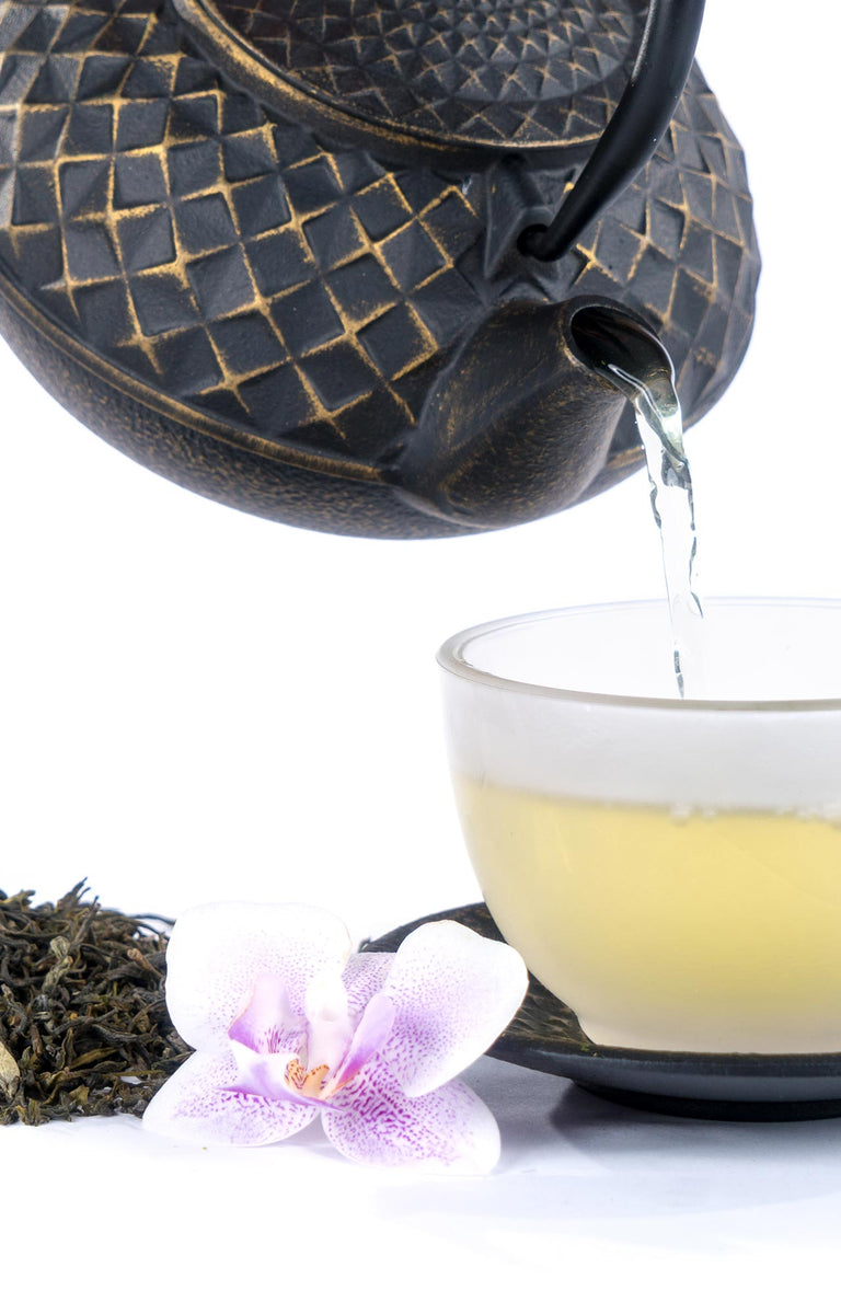 Detailansicht: Teekanne gießt grünen Tee in Glas-Tasse – grüner Tee bei tee-shopo.shop