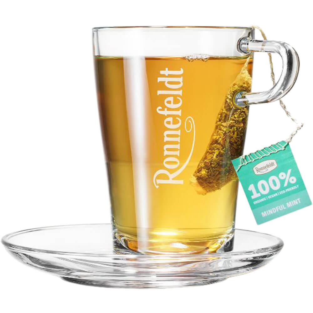 Ronnefeldt Premium Teebeutel Mindful Mint in Glastasse mit goldgelbem Kräutertee und Glasuntertasse