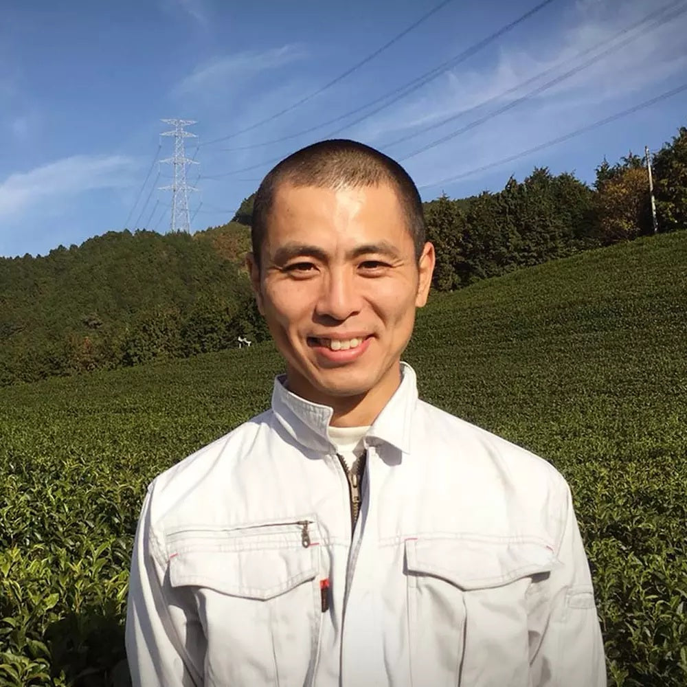 Der Produzent des Uji Matcha Premium Ookawa steht vor einem üppigen grünen Teefeld in der Region Uji, Japan.