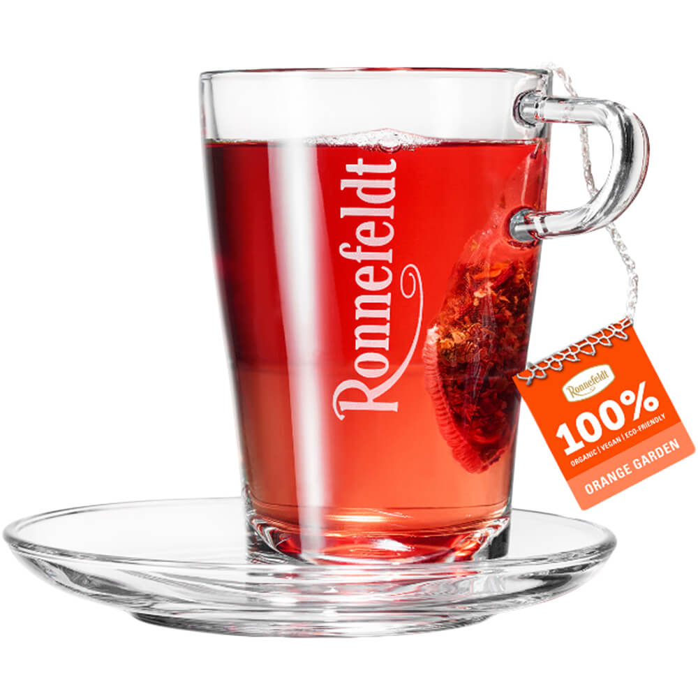 Orange Garden bio Früchtetee im Ronnefeldt Teeglas mit Untertasse, Teebeutel und orangefarbenem Fähnchen